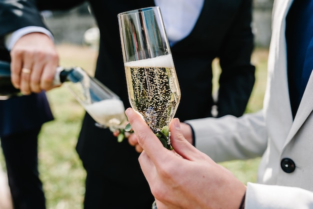Фото Жених наливает шампанское в бокал на фоне друзей на природе на свадебной церемонии close up toast