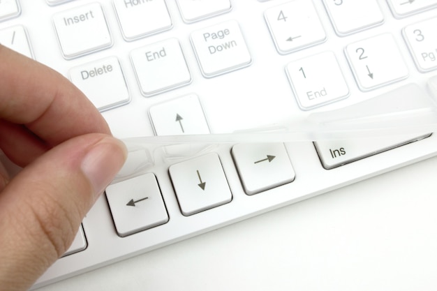 Фото Рука снимает с клавиатуры силиконовую пленку, защищающую ее от пыли и грязи. сохранение клавиатуры.