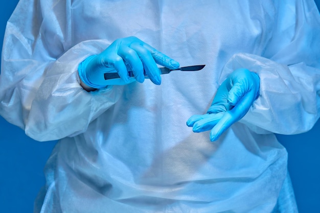 Фото Руки медицинского работника в форме и перчатках держат скальпель