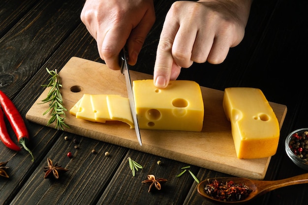 사진 요리사의 손은 칼로 치즈를 작은 조각으로 잘라서 절단판에서 맛보기 위해 맛있는 우유 치즈 레시피 프레젠테이션