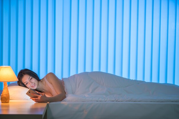 写真 幸せな女性はベッドと電話に横になりました。夕方の夜