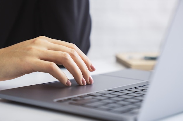 写真 画像は、オフィスの周囲を背景にぼかした状態で、高度なラップトップのキーボードを入力している女性の手の詳細を示しています