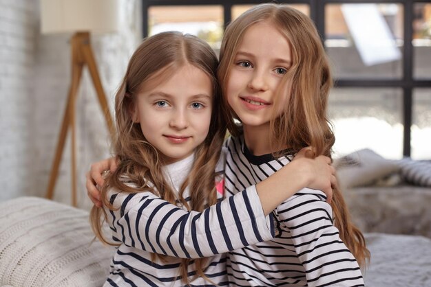Фото Изображение двух младших сестер, сидящих на кровати в комнате