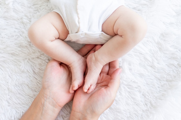 침대 클로즈업의 흰색 배경에 어머니의 손에 있는 갓난 아기의 다리, 어머니의 사랑과 보살핌