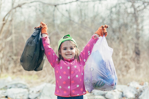 Фото Маленькая девочка собрала в лесу и парке два мешка с мусором и пластиковые бутылки, девочка рада, что помогла волонтерам убирать парк.