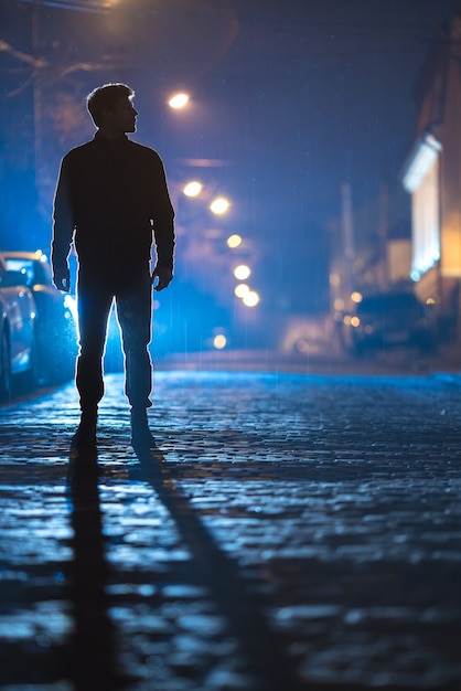 Мужчина стоит на дождевой дороге. вечер в ночное время. снимок с телеобъектива