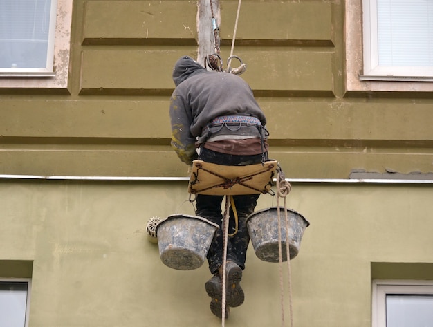 Фото Мужчина работает на высотных работах по штукатурке дома.