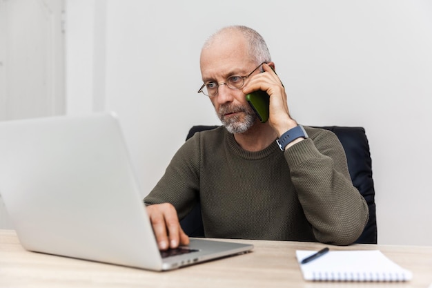 写真 老人はラップトップで作業し、携帯電話で話します