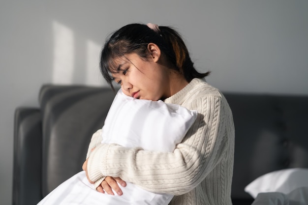 写真 悲しくて孤独な女性は ⁇ 自宅の寝室のベッドの上に枕を抱きしめています ⁇