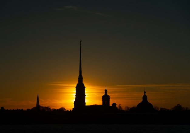 写真 空の黄色、オレンジ、赤の背景に夕日の光線でロシアのサンクトペテルブルクにあるピーターとポール要塞のシルエット