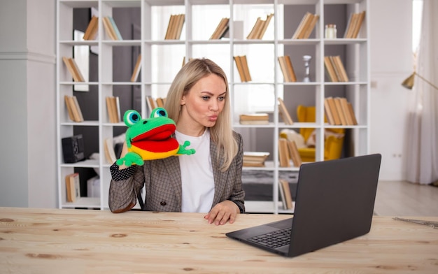 Фото Учитель-логопед проводит онлайн-урок удаленно с ноутбуком. женщина-логопед показывает упражнение с вязаной игрушкой-лягушкой.
