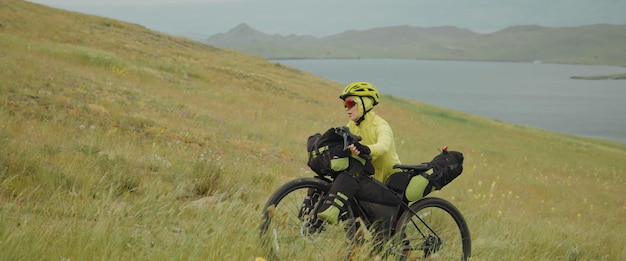 写真 上り坂で自転車を押すスポーツウーマンの旅行者の女性女性は自転車で旅行しますモダンなスタイルのスポーツウェアのヘルメットと緑と黒の色のスポーツメガネの自転車