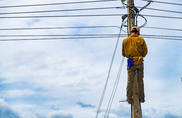 写真 技術者は電気問題を修理するために電柱に登っています。