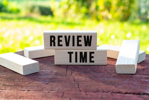 写真 ぼやけた庭の背景に古い木の切り株に横たわっている木製の立方体に「review time」というテキストが書かれています