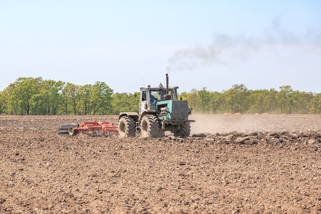 사진 트랙터는 경운기로 토양을 갈아서 침대의 덩어리를 부수고 봄 파종을 위해 밭을 준비합니다.