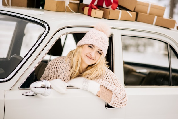 女性は、クリスマスツリーで飾られたレトロな車に乗って、雪に覆われた森の中でプレゼントをします。冬のクリスマスのコンセプト