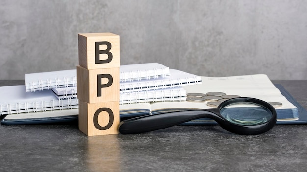 Фото Слово bpo написано на деревянных кубиках на сером фоне крупным планом деревянных элементов, увеличительных стеклянных бумажных документов