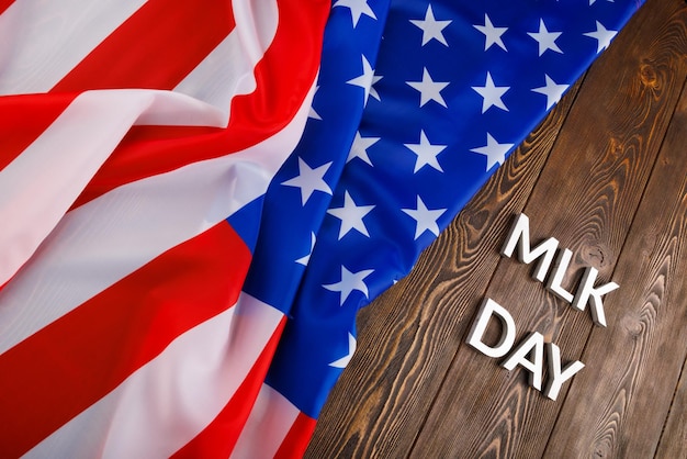 사진 mlk 데이라는 단어는 왼쪽에 구겨진 미국 국기가 있는 나무 표면에 은색 금속 글자로 놓였습니다.