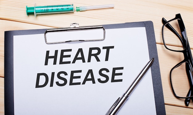 写真 heart diseaseという言葉は、黒い縁のメガネ、ペン、注射器の横にある白い紙に書かれています