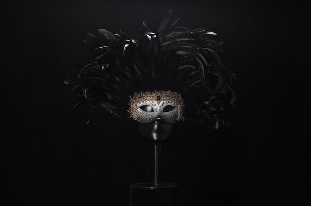 театральная маска с черными перьями на черном фоне