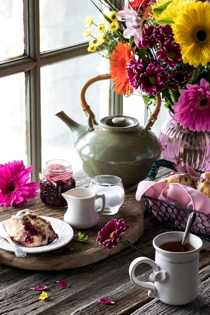 Foto thee en scones met een fel gekleurd bloemenboeket op een rustieke tafel