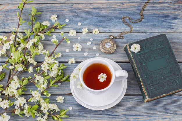 thee in een beker, oud boek, zakhorloge en kersentakken