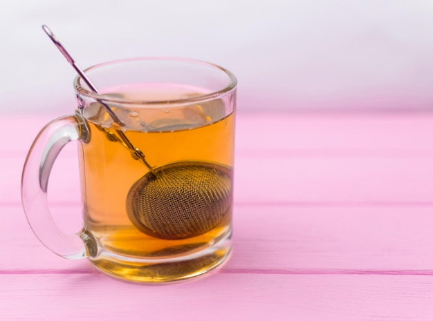 Foto thee in een glas met een theepotlepel op een roze houten achtergrond