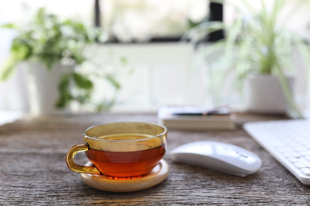 Thee in transparante glazen beker op houten tafel met muis en toetsenbord