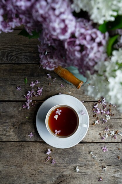 Thee in witte thee kopje, boeket van lila bloemen op oude houten tafel