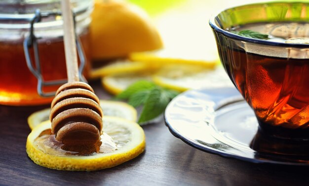 Thee met citroen en munt in de natuur. Een kopje hete muntthee met citroen en honing in pot. Citroenschijfjes en een lepel met honing tot hete thee.