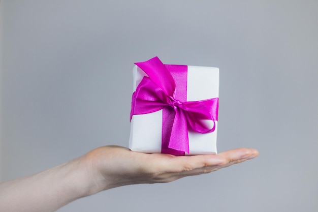 Theme of celebrations and gifts woman holding exclusive gift Packed in white box with purple ribbon beautiful and expensive gift on dark background