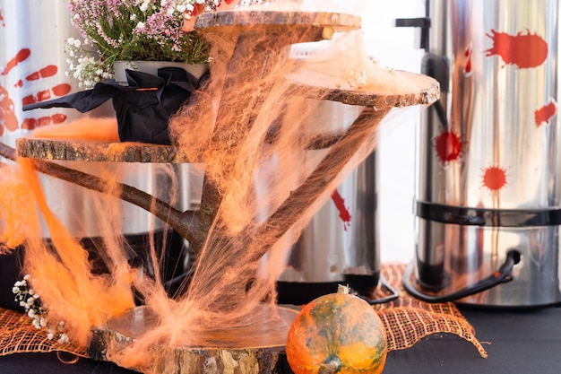 Themed decor for the traditional Halloween holiday. Drinks and sweet snacks on buffet festive party table, autumn maple leaves, Jack-o-lantern pumpkin and candles.