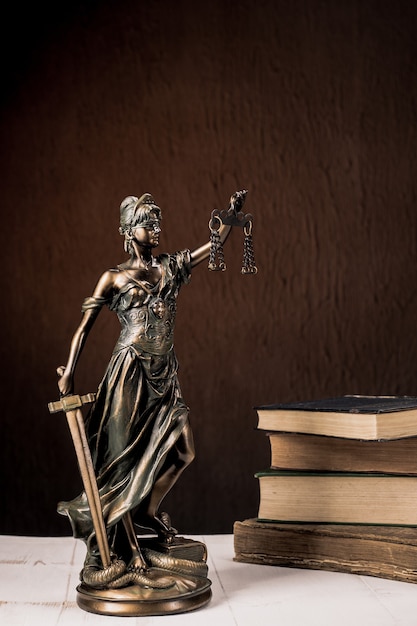 Themis figurine stands on a white wooden table next to a stack of old books. Scales Law Lawyer Business Concept. - Image