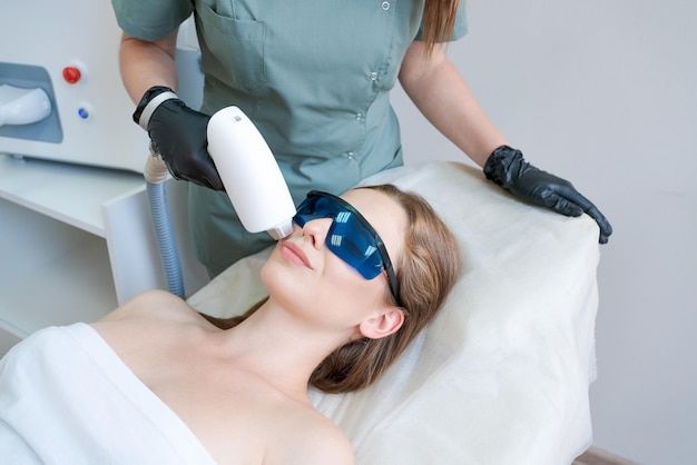 Therapeut schoonheidsspecialist ondergaat laserbehandeling op gezicht jonge vrouw in schoonheid