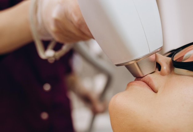 Foto l'estetista terapista fa un trattamento laser al viso di una giovane donna presso la clinica di bellezza spa procedure di epilazione per la depilazione laser facciale primo piano