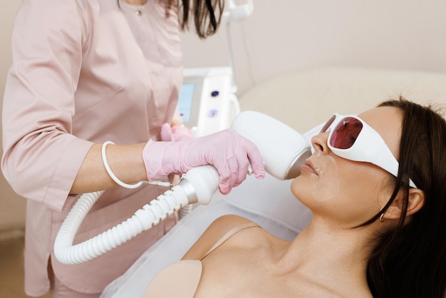 Foto l'estetista terapista fa un trattamento laser al viso di una giovane donna presso il laser facciale della clinica di bellezza