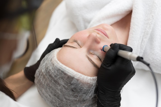 セラピスト美容師が美容SPAクリニックで若い女性の顔にレーザー治療を行う