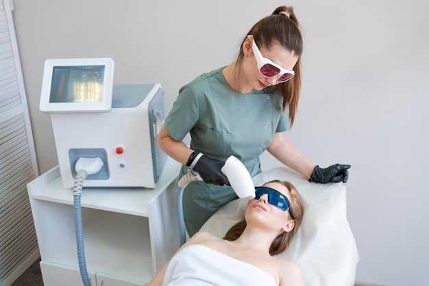 Therapist cosmetologist undergoes laser treatment on face young woman in beauty