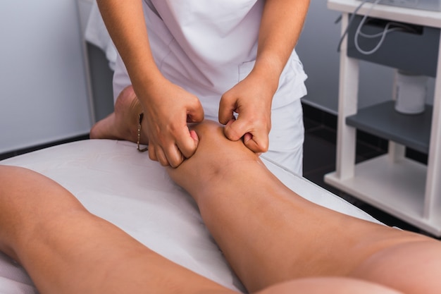 스파 센터에서 너클이 있는 여성에게 종아리 마사지를 하는 치료사. 마사지는 스파 살롱의 마사지 테이블에 있는 여성의 다리를 마사지합니다.