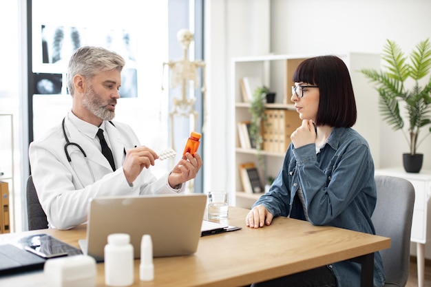 Therapist holding medications near woman in doctor's office