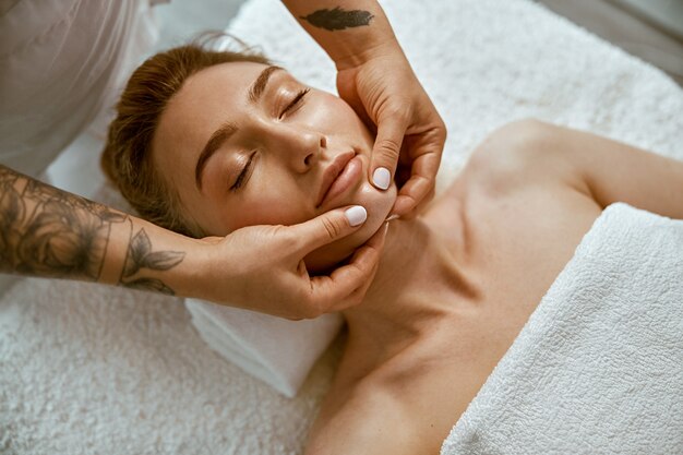 Therapist is doing face relaxing massage to a young woman in modern wellness cabinet