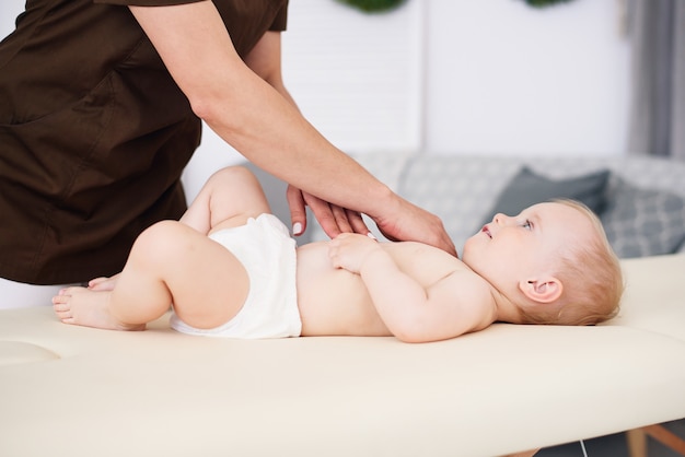 Il terapista fa massaggio a un bambino piccolo nella moderna e accogliente camera. concetto di assistenza sanitaria e medica.