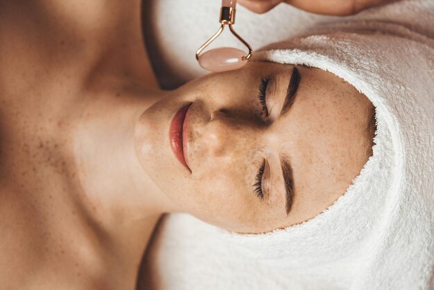 Terapista che massaggia il viso del paziente con il rullo di giada vista dall'alto sorriso soddisfatto massaggio della pelle perfettamente luminoso