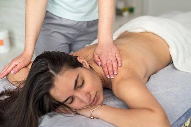 Therapist performs a professional hand massage of the back and shoulders of a young beautiful woman lying down and enjoying the procedure