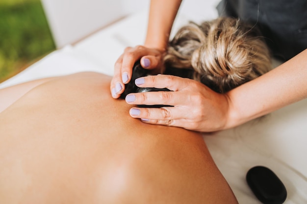 Therapist placing hot spa volcanic lava stone on a female\
patient\'s neck and back energy stones