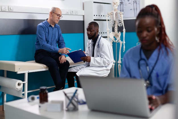 Therapist practitioner doctor explaining disease expertise to retired old man discussing healthcare treatment in hospital office. Senior patient having medical consultation. Medicine concept