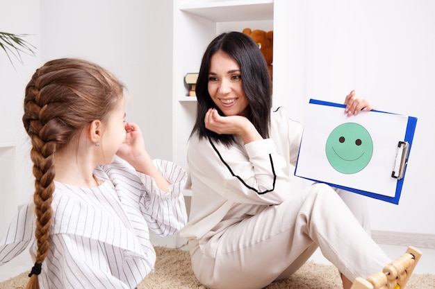 Terapeuta che mostra al piccolo paziente il volto sorridente sulla carta. concetto di psicologo.