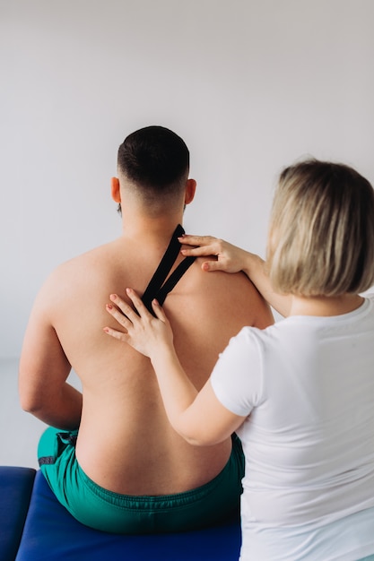 A therapist taping kinesiology tape on patients neck.