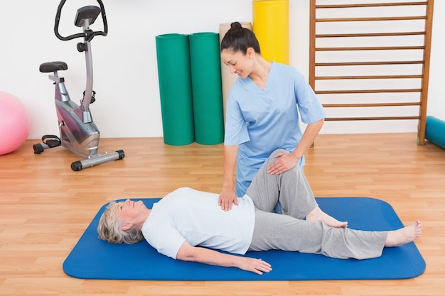 Therapist working with senior woman on exercise mat 