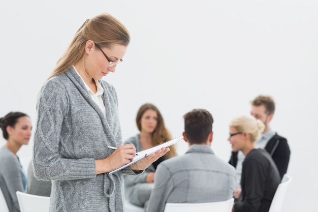 Therapist writing notes with group therapy in session